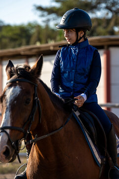 Young girl riding bay horse during equestrian lesson outdoors