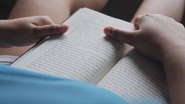 Close-up macro shot of a woman's fingers gently turning a page of an open book, with shallow depth of field, soft natural window light, and blurred background creating a dreamy intimate mood.
