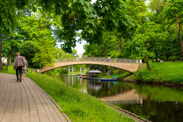 people walking along canal path near arched bridge in city park © Boriss