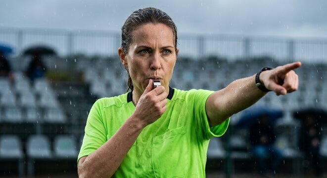 Professional female soccer referee making decisive call during rainy match