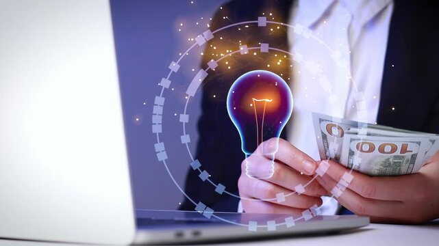 Business person holding money while using laptop to explore new ideas in a modern office setup during daytime.