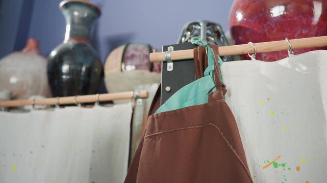 Artist fixing apron before lesson. Ceramic artist adjusting apron as sunlight illuminates workspace. Vibrant pottery studio with artist securing apron amid glazed vases and warm sunlight