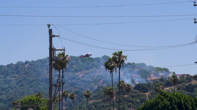 Slow motion shot of Los Angeles Fire Department responding to wildfire with aerial unit dropping water 