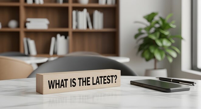Seeking Current Updates A wooden block inscribed 'WHAT IS THE LATEST?' on a modern desk, symbolizing inquiry and the pursuit of fresh information