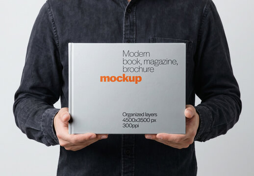 Hardcover Book Mockup Held Horizontally With Both Hands By Man Front View On Light Background
