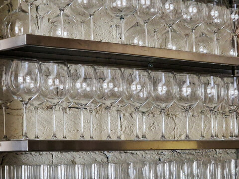Empty wine glasses arranged on metal shelves in a bar.