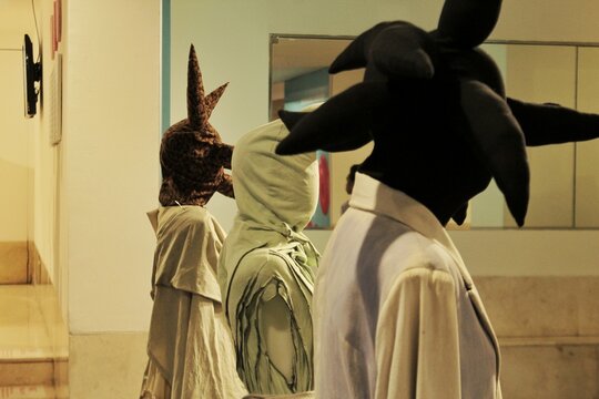 A captivating view of a contemporary art installation inside a gallery, featuring mysterious figures or mannequins wearing unique, surreal, and avant-garde masks.
