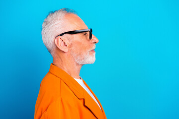Senior man in orange jacket and sunglasses profile portrait on bright blue background, stylish elderly model with white beard and modern eyewear © deagreez