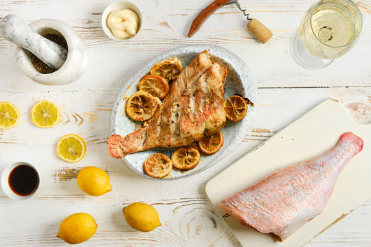 Grilled red snapper served on a dish with lemons and sauce on a wooden table