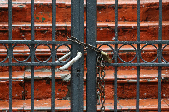 Closed and locked metal gate with chain and padlock in front of red concrete stairs.