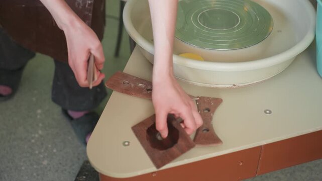 Pottery workshop wheel tools neatly arranged. Hands placing templates, cardboard guides and trimming pieces beside idle potters wheel, neat studio table with sponge and bat, instructional tidy setup