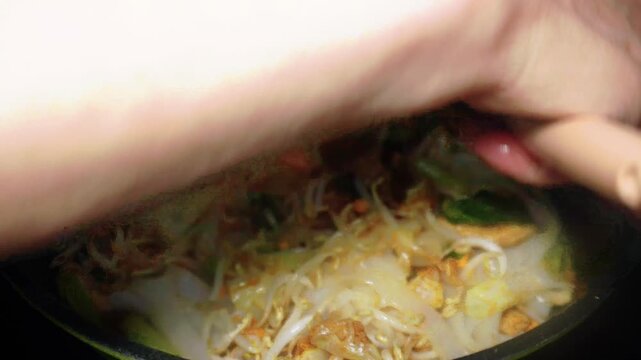 The process of cooking special homemade stir-fried flat rice noodles (Kwetiau Goreng). The flat noodles are cooked with eggs, bean sprouts, bok choy, cabbage, and sliced meatballs