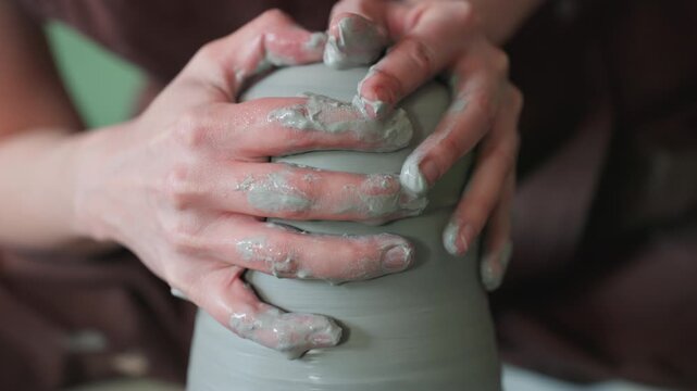 Closeup hands shaping clay on wheel, intimate studio scene showing wet fingers centering tall clay column, slow rhythmic motions, textured surface, artisan focus and calming atmosphere