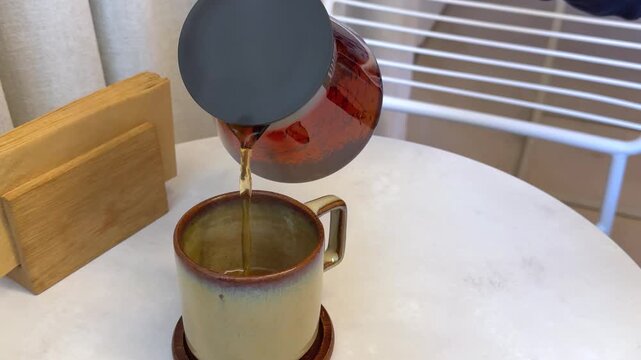 Transparent glass teapot with deep golden brown tea ready for serving and relaxation