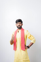 Fototapeta premium Smiling young Indian man in traditional yellow kurta giving a thumbs up pose in a studio portrait.