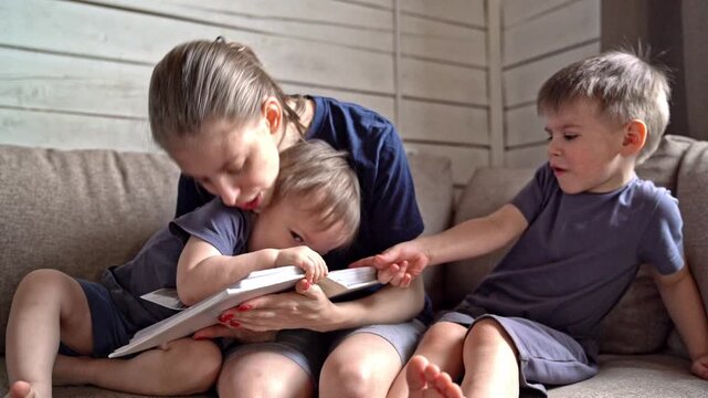 White mother comforting son between pages on couch while younger white child flips album, soft gestures and close embrace create symbolic reassurance, gentle mood of protection and shared family