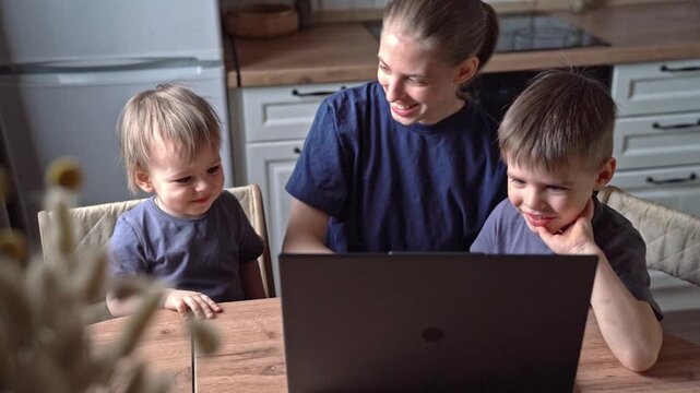 White mother and sons smiling at laptop together in kitchen, shared laughter, tech bridging distance, warm emotional connection, candid moment, playful reactions, sunlight warmth, gentle eye contact,