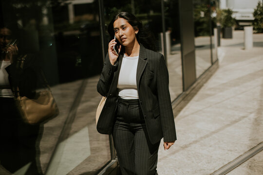 Businesswoman walks and talks on phone outside modern building in city during daytime