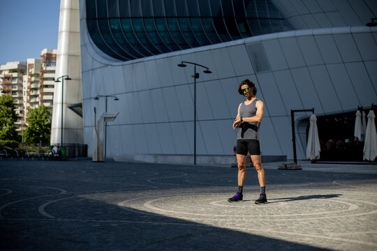 Sporty individual checking watch in modern urban landscape under bright sun