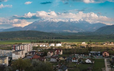 Fototapeta premium Breathtaking scenery unfolds as snow-capped mountains rise above a charming village during dusk. Homes dot the landscape while lush fields stretch towards the horizon, creating tranquility