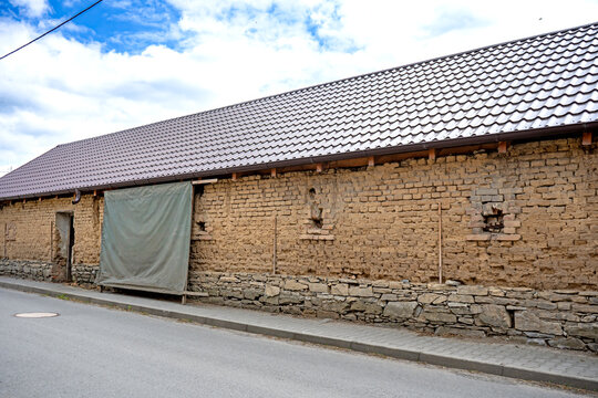 Old rural clay brick wall with tiled roof along village street stara stena  obec Blatec, Czech Republic - May 10, 2026