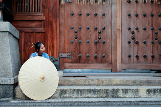 Young Woman in Blue Kimono Behind Paper Umbrella at Japanese Shrine Gate