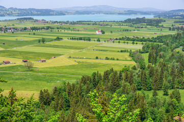 Obraz premium Scenic Bavarian landscape with rolling green fields, a lake, and distant mountains