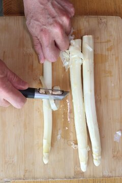 Peeling white asparagus to remove the outer layer of cellulose, preparing it for cooking.