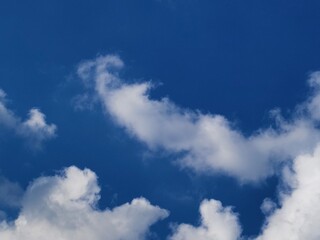 Fototapeta premium Beautiful fluffy white cumulus clouds scattered across a deep blue sky on a bright sunny day. Natural sky background template with copy space