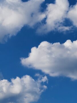 Beautiful fluffy white cumulus clouds scattered across a deep blue sky on a bright sunny day. Natural sky background template with copy space