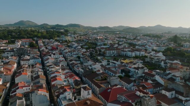 Aerial view over the dense urban fabric of Ponta Delgada, featuring a sea of traditional white buildings with terracotta roofs stretching towards the volcanic hills in the distance, S o Miguel Island