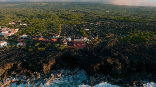 Aerial view of a coastal village on Pico Island, Azores, with traditional houses situated on rugged black lava rock cliffs overlooking the Atlantic Ocean.