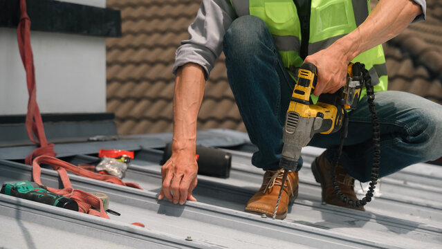 Close Up of Roofer Using Power Drill for Metal Roof Repair and Maintenance on Residential Building