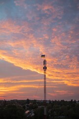 Obraz premium Telecommunications tower against the backdrop of a cityscape at sunset, Ukraine. Ukrainian flag on a telecommunications tower at sunset.