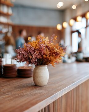 Warm cafe aesthetic with colorful autumn leaves arrangement on wooden bar counter, blurred customers and golden lighting