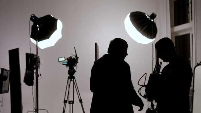 Silhouetted figures of a film crew working under professional studio lighting with camera equipment. Concept of filmmaking, media production, and backstage work environments.