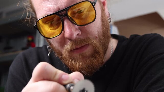 Worker in protective eyewear sharpening a small circular saw cutting disc clamped in a vise