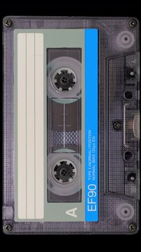 Vintage Audio Cassette Reels Spinning. Retro compact cassette tape with spinning reels on black background.	