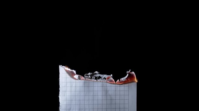 Checkered graph paper slowly burns from the top edge until the flames turn into rising smoke. Concept of destroying evidence, failed projects, and erasing physical data completely.