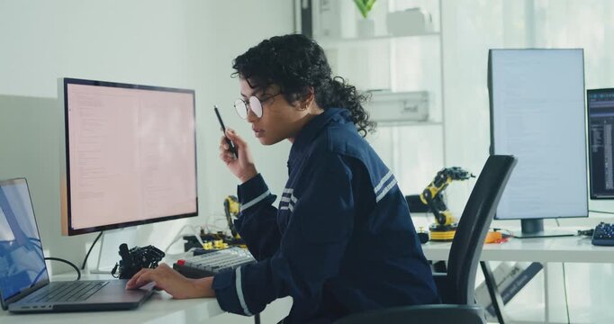 Young African American female robotics engineer coding AI software for robotic arm in laboratory. Embedded system, firmware testing, machine learning, industrial automation, future technology concept.