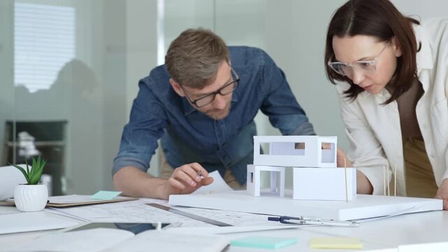 Architects are discussing and analyzing a new housing project, working together on a scale model and technical drawings while planning future construction ideas