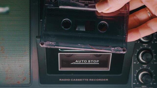 A close up of a hand inserting a transparent audio cassette into a retro radio recorder and closing the deck. Concept of nostalgia, 80s music, vintage technology, and analog audio.