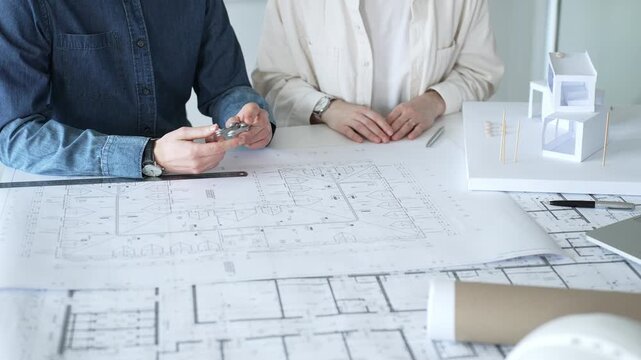 Engineering professionals collaborating on an architectural blueprint, using a compass to design a modern building, planning construction with a house model and laptop