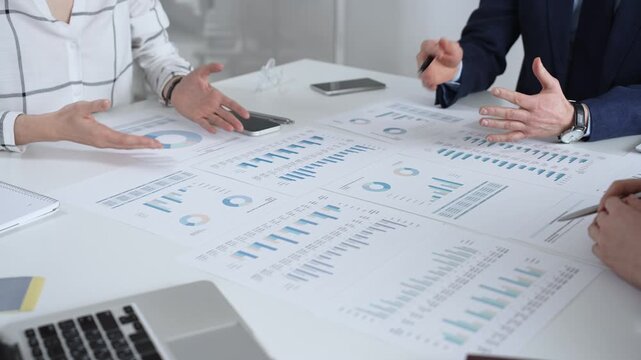 Business team in a conference room reviewing financial reports, charts and graphs across the table, collaborating on strategy, investment planning and growth initiatives