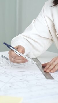 Female architect or engineer working on blueprints using a compass and ruler. Designing building plans. With a yellow hard hat and tablet on the desk