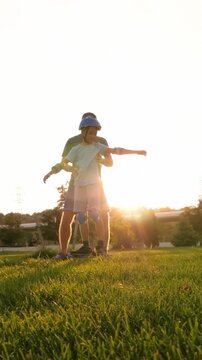Father teaches son roller skating in park. Child practices balance on skates under sunny sky. Vertical composition capturing skill development, mentorship and active learning outdoors.