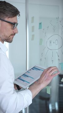 Business professional planning project strategy, analyzing data on a tablet, and collaborating on a glass whiteboard with flowcharts and sticky notes in a modern office