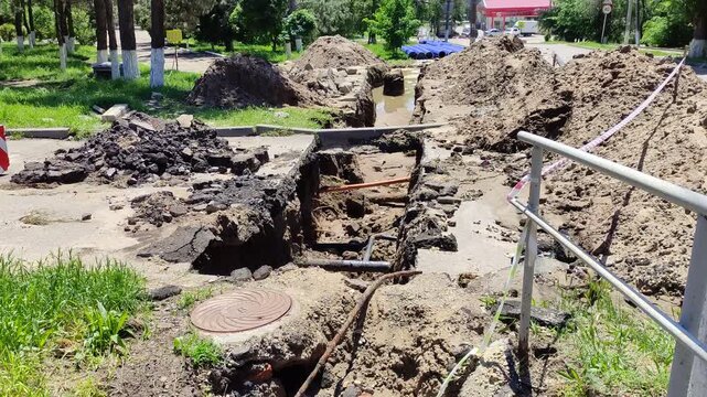 Large trench dug in asphalt road with piles of dirt and manhole cover, vertical video