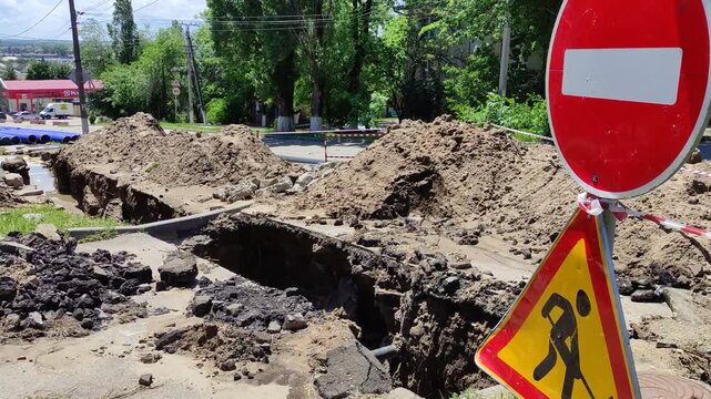 Road construction trench with dirt piles and red warning signs close up