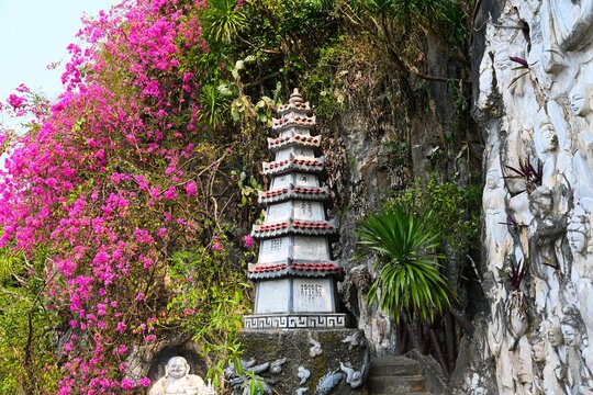 DA NANG, VIETNAM - APRIL 15, 2026:Stone pagoda tower surrounded by beautiful marble reliefs and blooming pink bougainvillea flowers on a cliff at Marble Mountains in Da Nang Vietnam